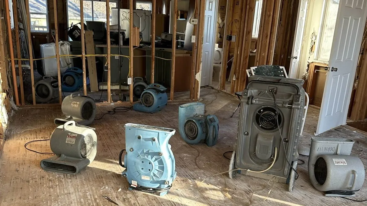 Air movers and a dehumidifier drying a gutted room during water damage restoration in Nassau County