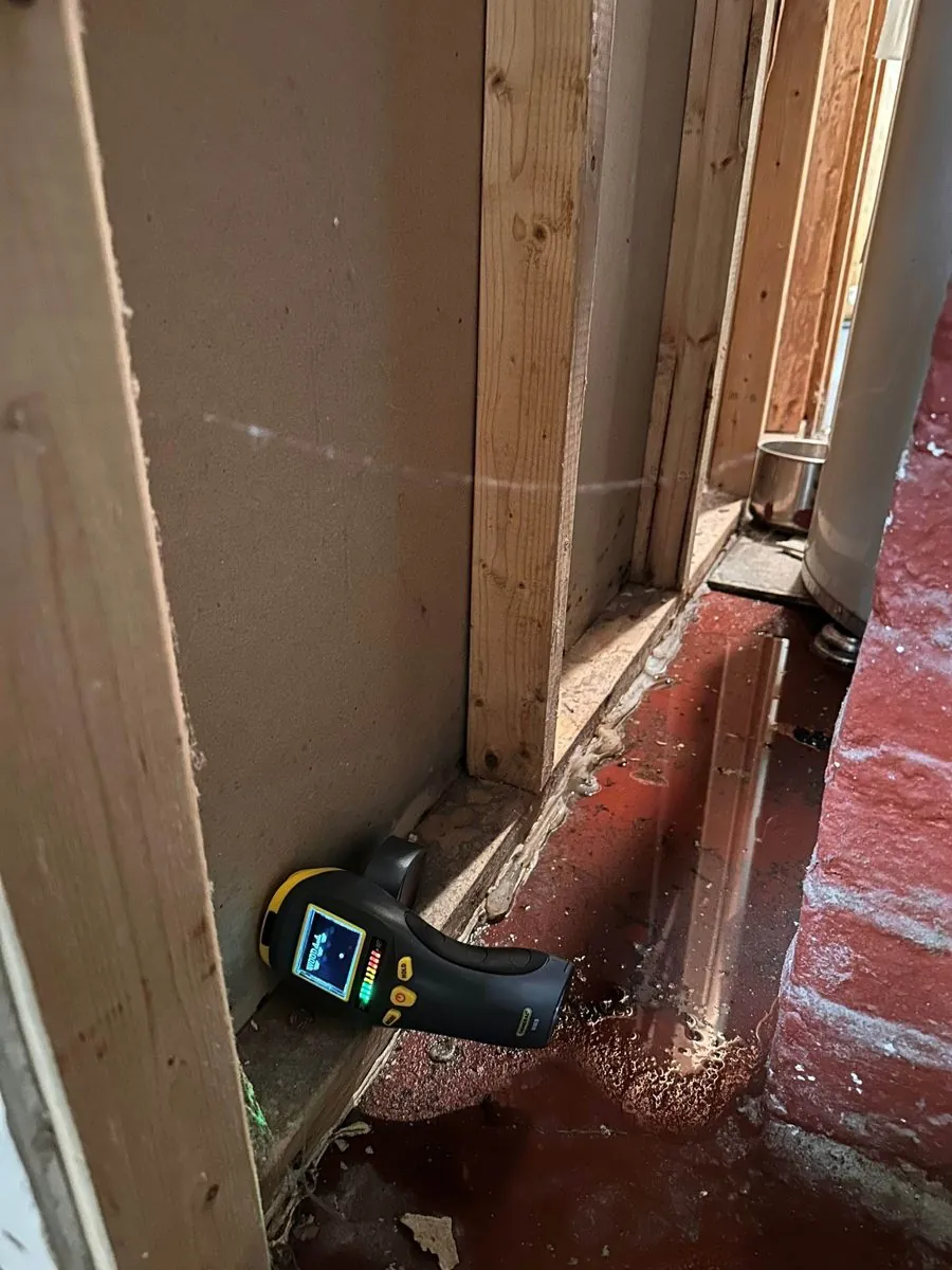 Checking a baseboard for hidden moisture with a thermal camera during a water damage inspection in Brooklyn
